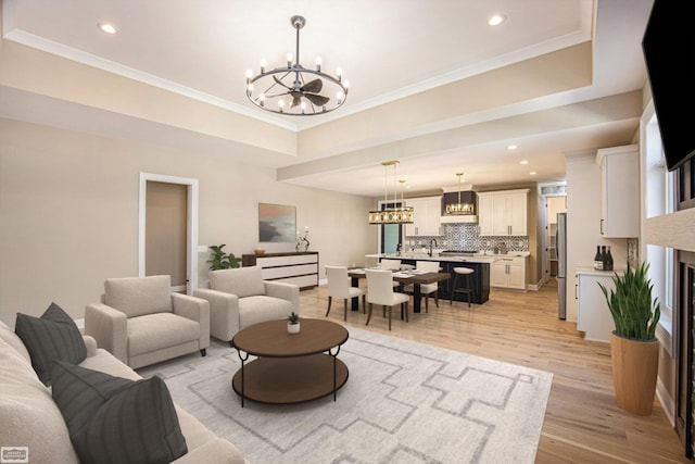 living room featuring light wood-type flooring, a chandelier, sink, a raised ceiling, and ornamental molding