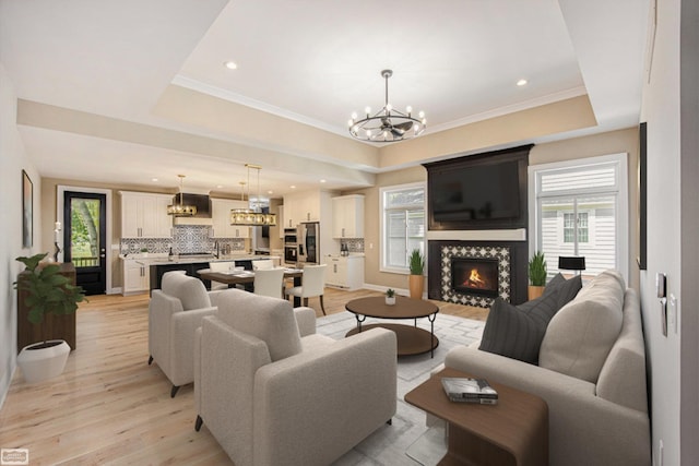 living room featuring ornamental molding, a notable chandelier, light wood-type flooring, and a raised ceiling