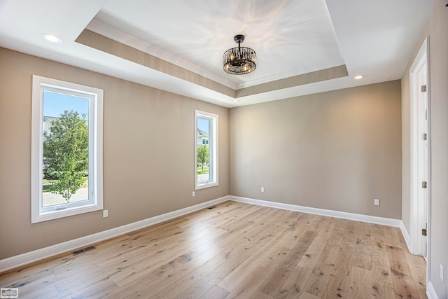 spare room featuring an inviting chandelier, light wood-type flooring, and a raised ceiling