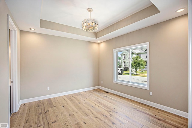 unfurnished room featuring light hardwood / wood-style flooring, a tray ceiling, and an inviting chandelier