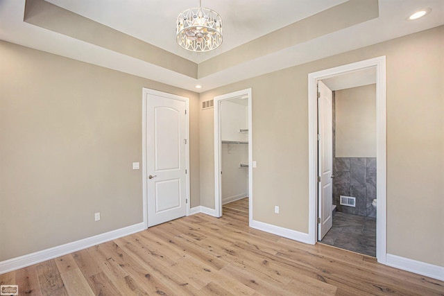 unfurnished bedroom featuring a raised ceiling, connected bathroom, light hardwood / wood-style floors, and a spacious closet