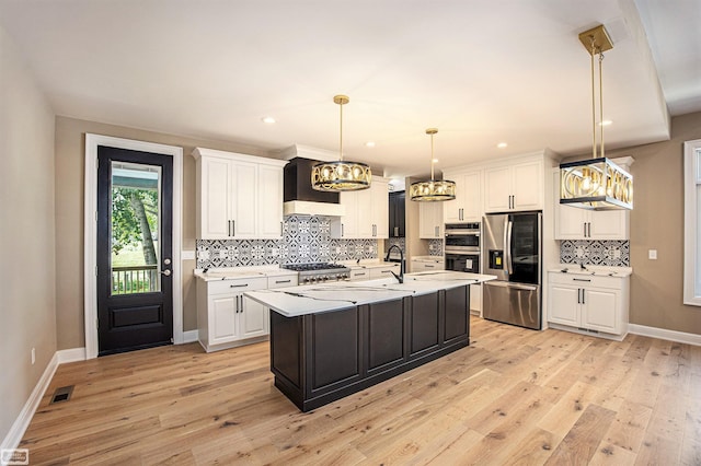 kitchen featuring custom range hood, white cabinets, stainless steel appliances, light hardwood / wood-style flooring, and a kitchen island with sink