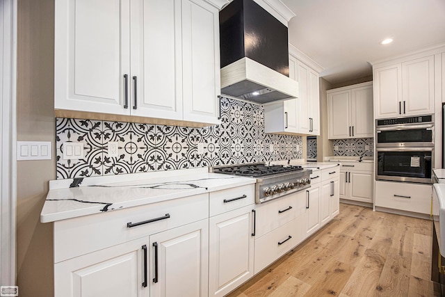 kitchen with custom range hood, white cabinetry, backsplash, stainless steel appliances, and light hardwood / wood-style flooring