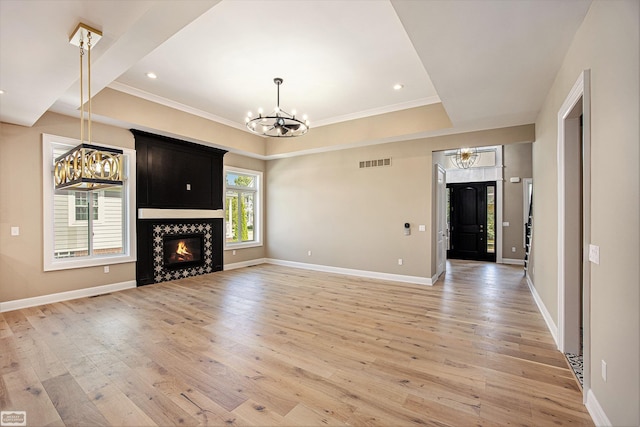 unfurnished living room with a high end fireplace, light hardwood / wood-style floors, a tray ceiling, an inviting chandelier, and crown molding