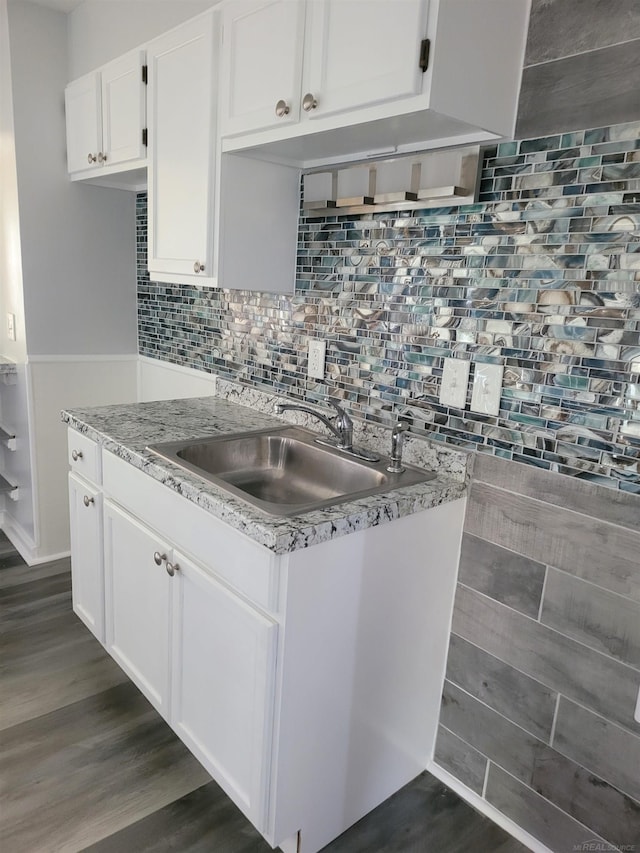 kitchen with dark wood-type flooring, white cabinets, backsplash, light stone countertops, and sink