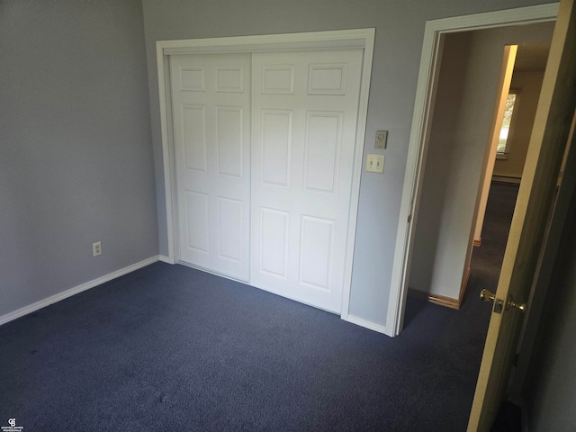 unfurnished bedroom featuring a baseboard radiator, a closet, and dark colored carpet