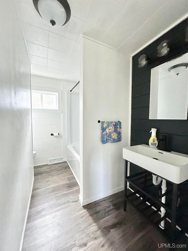 interior space with tub / shower combination, toilet, and hardwood / wood-style flooring