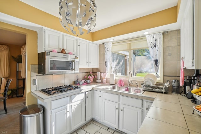 kitchen with appliances with stainless steel finishes, white cabinetry, light tile patterned floors, tile countertops, and sink