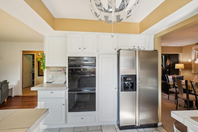 kitchen featuring stainless steel fridge, white cabinetry, black double oven, and tile countertops