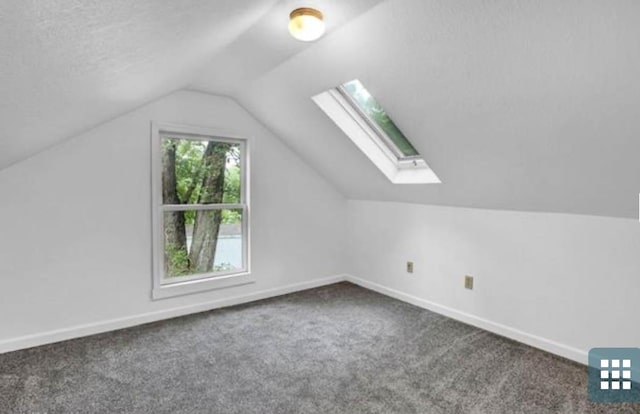 additional living space with a textured ceiling, vaulted ceiling with skylight, and dark colored carpet