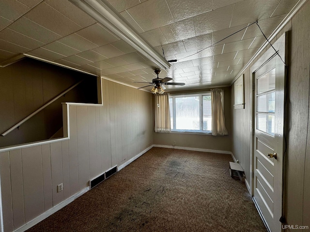 carpeted empty room with wooden walls and ceiling fan