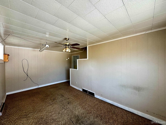 spare room featuring ceiling fan, wooden walls, and dark colored carpet