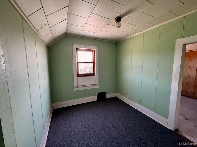 carpeted spare room featuring wooden walls and vaulted ceiling