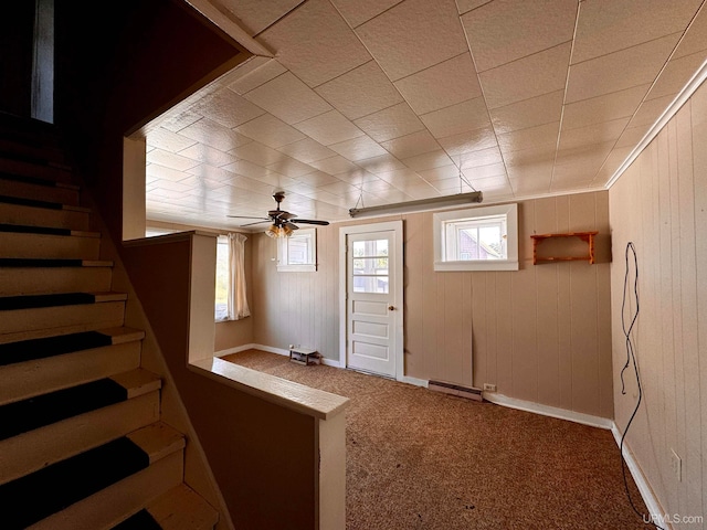 interior space with ceiling fan, wooden walls, baseboard heating, and carpet flooring