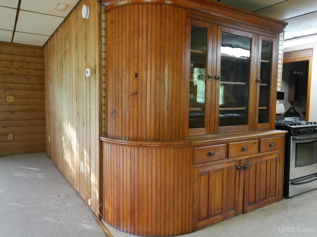 interior space featuring light colored carpet, gas range, wooden walls, and a paneled ceiling