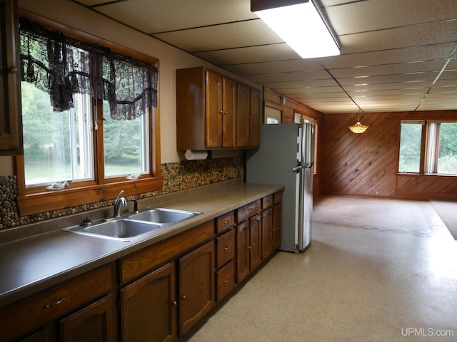 kitchen with stainless steel refrigerator, wooden walls, sink, and a healthy amount of sunlight