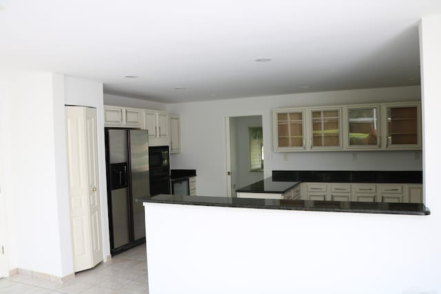 kitchen featuring black microwave, kitchen peninsula, light tile patterned floors, and stainless steel fridge