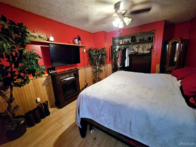 bedroom featuring ceiling fan, wood walls, a textured ceiling, a closet, and hardwood / wood-style floors