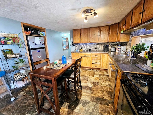 kitchen featuring decorative backsplash, black gas range oven, stainless steel refrigerator, a textured ceiling, and sink