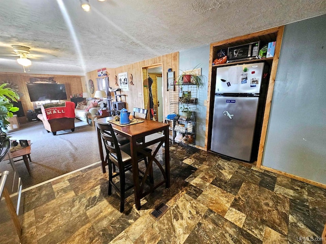 carpeted dining space with wooden walls, ceiling fan, and a textured ceiling