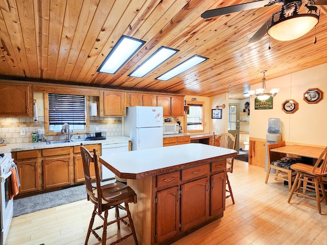 kitchen featuring a skylight, hanging light fixtures, white appliances, a kitchen island, and light hardwood / wood-style floors