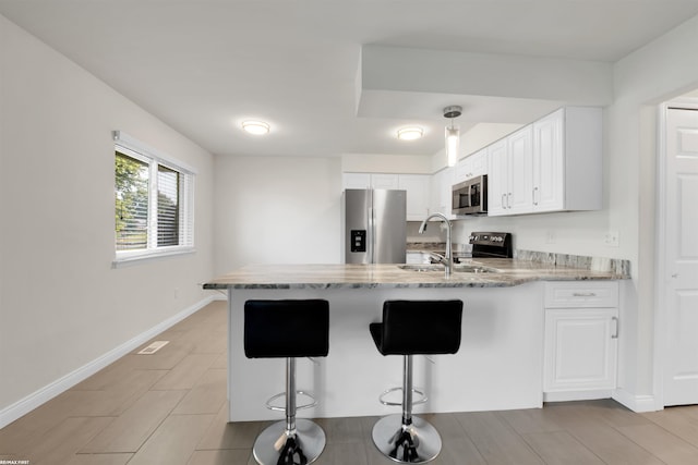 kitchen featuring appliances with stainless steel finishes, a kitchen bar, white cabinetry, and kitchen peninsula