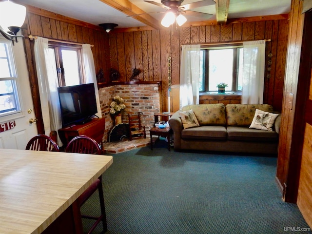 living room featuring wood walls, ceiling fan, beamed ceiling, and carpet floors