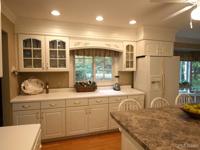 kitchen featuring white refrigerator with ice dispenser, white cabinets, ceiling fan, ornamental molding, and light hardwood / wood-style floors