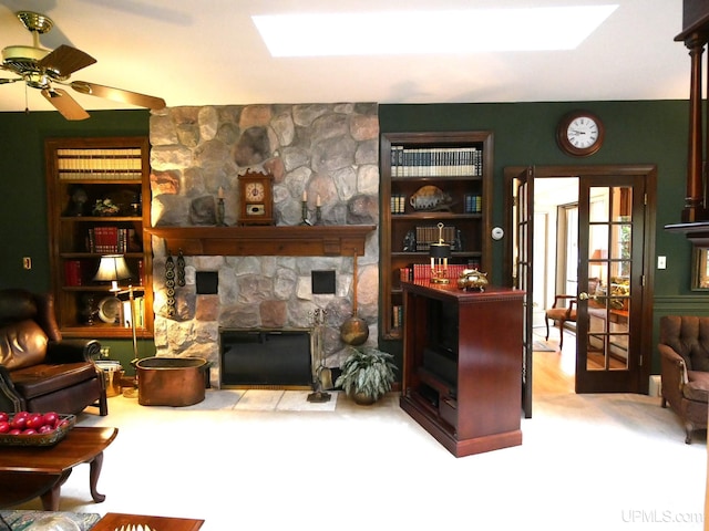 carpeted living room with ceiling fan, a stone fireplace, and french doors