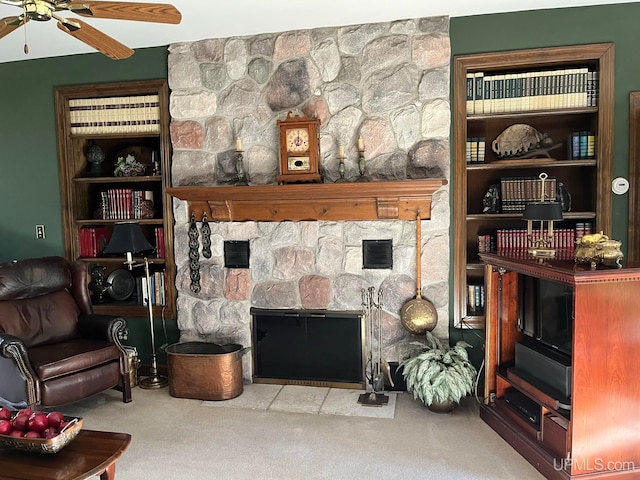 carpeted living room featuring a stone fireplace and ceiling fan