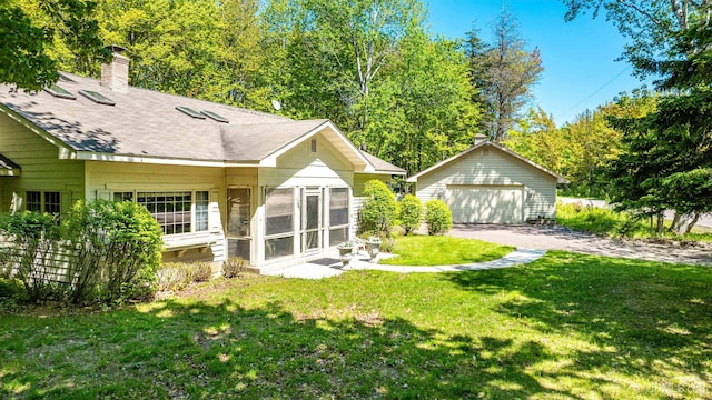 rear view of property featuring a sunroom, a garage, an outdoor structure, and a yard