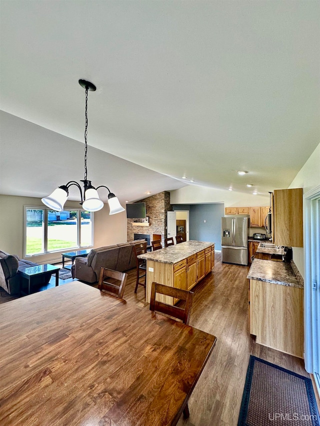 dining space featuring an inviting chandelier, lofted ceiling, a fireplace, and dark hardwood / wood-style flooring