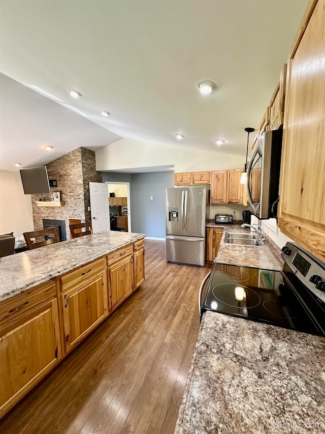 kitchen with appliances with stainless steel finishes, hanging light fixtures, vaulted ceiling, a stone fireplace, and hardwood / wood-style floors