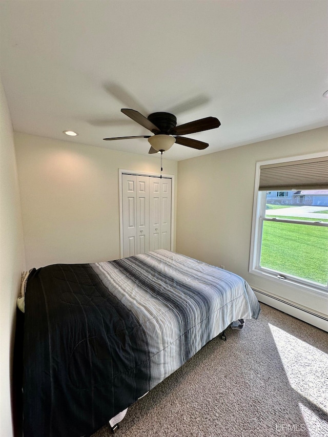 bedroom with a baseboard heating unit, a closet, ceiling fan, and carpet floors