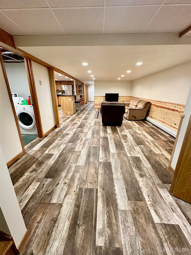 interior space with hardwood / wood-style flooring, a drop ceiling, wood walls, and washer / dryer