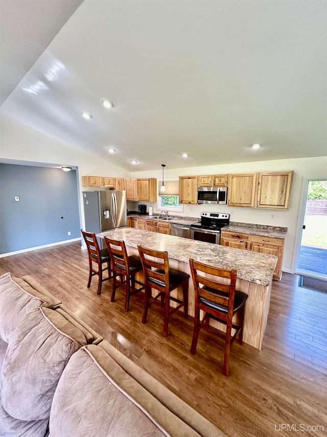 kitchen with appliances with stainless steel finishes, vaulted ceiling, a breakfast bar area, dark hardwood / wood-style flooring, and pendant lighting