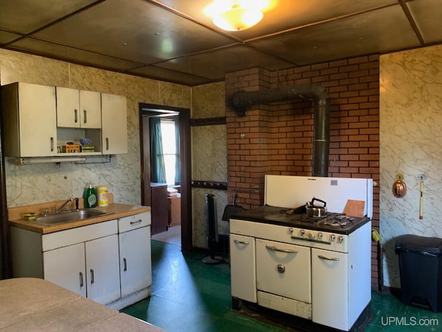 kitchen with a wood stove, white cabinets, white gas range oven, and sink