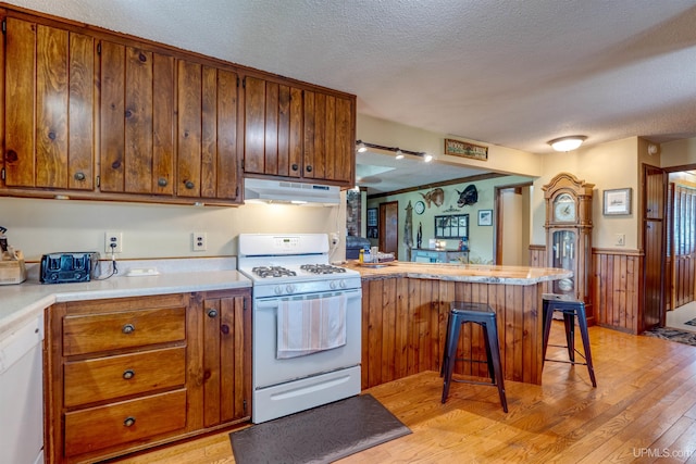 kitchen featuring light wood-type flooring, a textured ceiling, kitchen peninsula, a kitchen bar, and white appliances