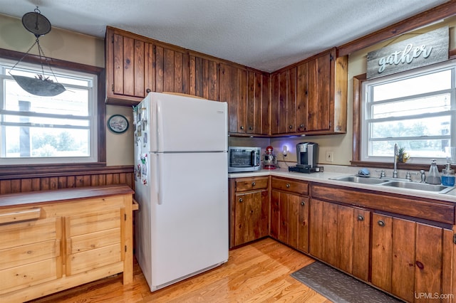 kitchen featuring sink, a textured ceiling, decorative light fixtures, light hardwood / wood-style flooring, and white fridge