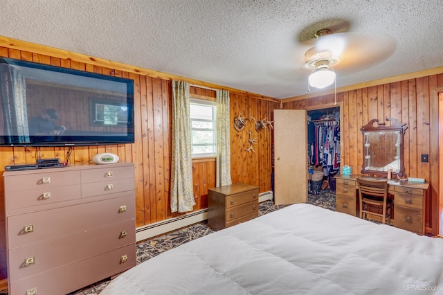 bedroom with a closet, wooden walls, baseboard heating, a spacious closet, and ceiling fan