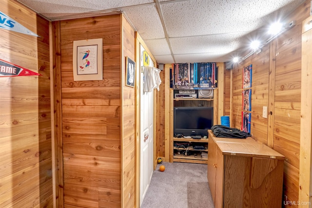 interior space featuring a drop ceiling, wooden walls, and light colored carpet