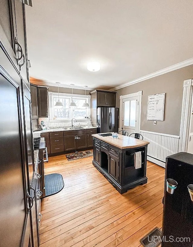 kitchen with dark brown cabinetry, pendant lighting, a kitchen island, light hardwood / wood-style flooring, and stainless steel fridge with ice dispenser