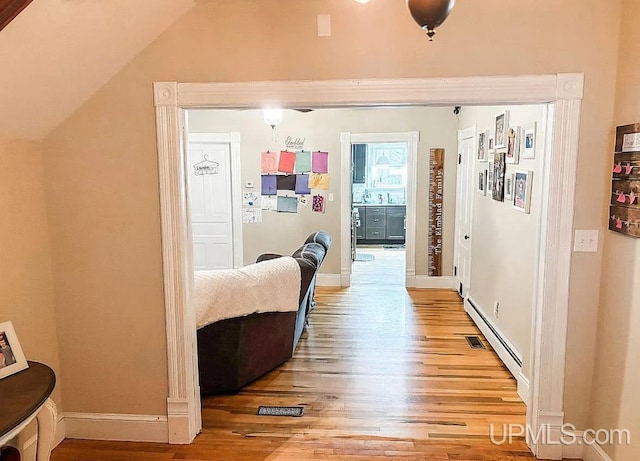 hallway featuring hardwood / wood-style flooring, a baseboard radiator, and vaulted ceiling