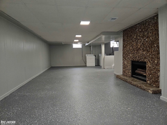 basement featuring a paneled ceiling, a large fireplace, and washer / dryer