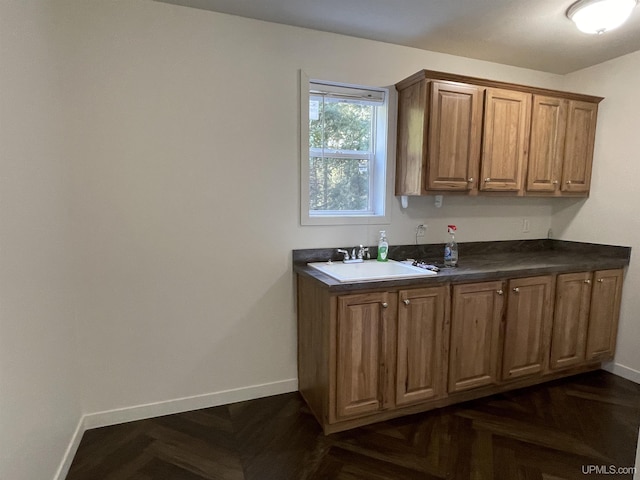 kitchen featuring brown cabinetry, a sink, baseboards, and dark countertops