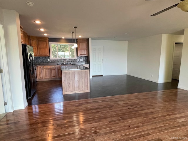 kitchen with hanging light fixtures, a kitchen island, black refrigerator with ice dispenser, ceiling fan, and dark hardwood / wood-style floors