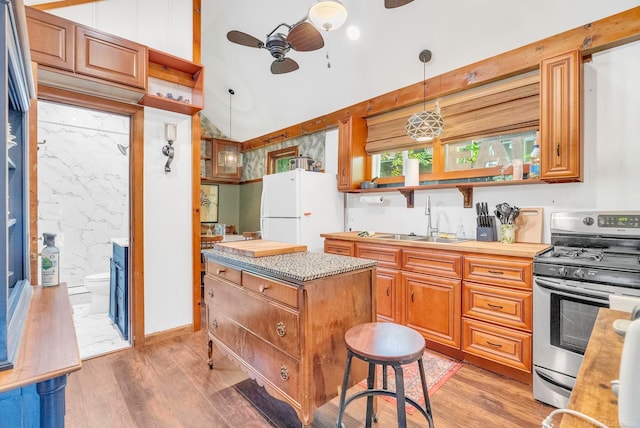 kitchen featuring stainless steel range with gas cooktop, sink, hanging light fixtures, white fridge, and ceiling fan