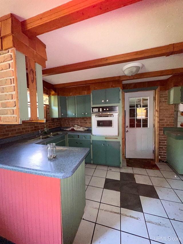 kitchen featuring light tile patterned flooring, beamed ceiling, white oven, green cabinetry, and kitchen peninsula