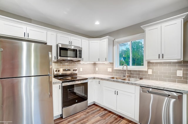 kitchen featuring white cabinets, sink, appliances with stainless steel finishes, light hardwood / wood-style floors, and decorative backsplash