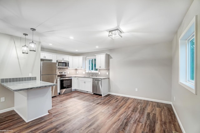 kitchen with sink, kitchen peninsula, white cabinetry, hardwood / wood-style flooring, and appliances with stainless steel finishes